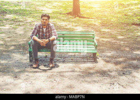 Junge hipster Mann sitzt auf einer Holzbank im Park. Stockfoto