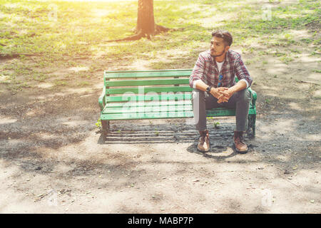 Junge hipster Mann sitzt auf einer Holzbank im Park. Stockfoto