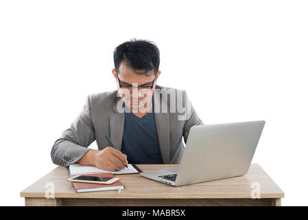 Geschäftsmann schreiben Notizen auf einem Schreibblock, während an seinem Schreibtisch hinter seinem neuen Notebook auf weißem Hintergrund sitzen. Stockfoto
