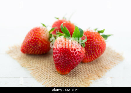 Frische Erdbeeren auf sackleinen und weißem Holz Hintergrund mit selektiven Fokus Stockfoto