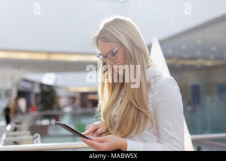Gerne blonde Geschäftsfrau news Lesen auf digitalen Tablet in Financial Center Stockfoto