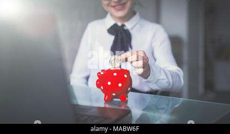 Junge Geschäftsfrau drop Bitcoin in roten gepunkteten Sparschwein, cineastische Stil Stockfoto
