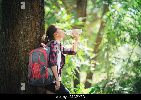 Durstigen Frau mit einer Unterbrechung trinken eine Flasche Wasser bei Wanderungen durch die Wälder. Stockfoto