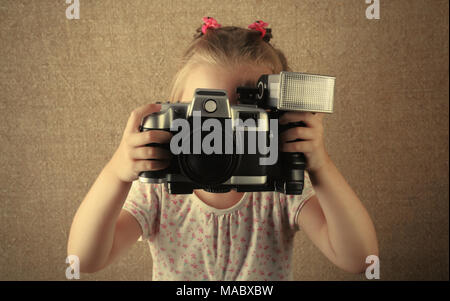 Die fröhliche kleine Mädchen der Fotograf mit der Kamera in den Händen. Es wird in einem Jahrgang alte Foto stilisierte Stockfoto