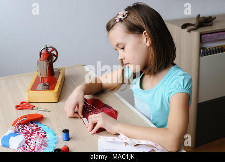 Das Mädchen ist das Nähen eines Kleides für eine Puppe. Sie mit einem Maßband, das Produkt zu messen. Stockfoto