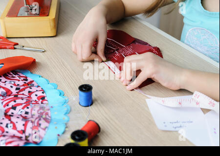 Ein Mädchen ist das Nähen eines Kleides für eine Puppe. Sie mit einem Maßband, das Produkt zu messen. Stockfoto