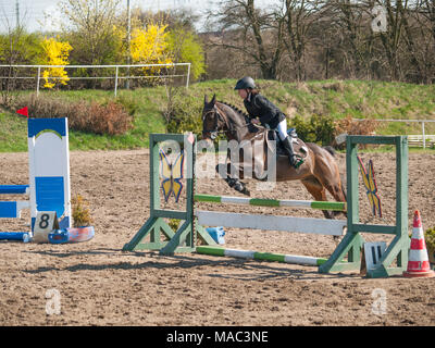 Ein Mädchen, das kaukasische Pferd Reiter reiten und springen eine Hürde mit ihren schönen braunen sport Pony Stockfoto