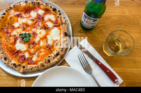 Pizza mit Mozzarella, Tomaten, gekochten Schinken und Basilikum, mit einem Peroni italienischen Bier Stockfoto