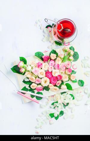 Feder lesen Konzept mit offenem Buch auf weißem Hintergrund mit Blumen, Rosenblätter, rosa Schreibwaren und Kräutertee. Feminine flach mit Kopie spa Stockfoto