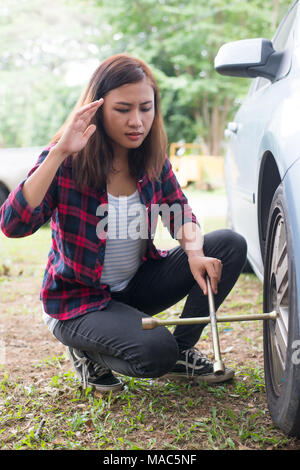 Junge hipster Frau Auschecken einer Reifenpanne auf Ihr Auto versuchen zu beheben. Stockfoto