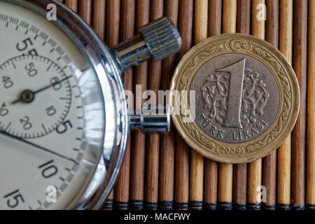 Stoppuhr und Münze mit einer Stückelung von einem türkischen Lira auf hölzernen Tisch Hintergrund Stockfoto