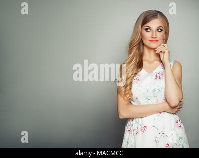 Schöne Frau mit blonden Wellig Frisur und Make-up Suchen auf Grau Banner Hintergrund. Perfekte Mode Modell tragen weiße Kleid Stockfoto