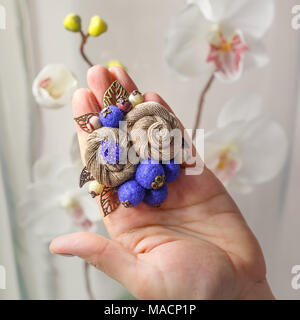 Kleine handgefertigte Brosche in Form von zwei beige Blumen liegt auf der Handfläche eine Frau Stockfoto