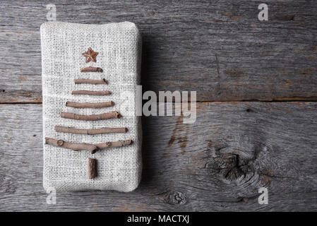 Overhead shot eines Sackleinen gewickelt Weihnachtsgeschenk mit einem Zweig, Baum und Stern auf einem rustikalen Holztisch, mit kopieren. Stockfoto