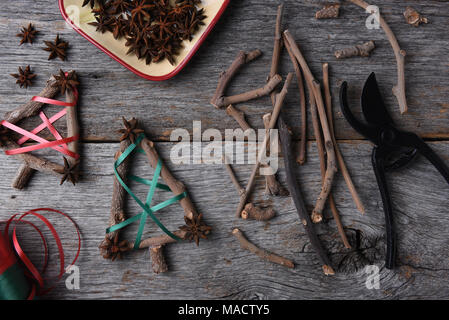 Ansicht von oben auf die Geräte und Materialien für die rustikale Weihnachtsschmuck, einschließlich Zweige, Sternanis, Scheren, und Farbband. Stockfoto