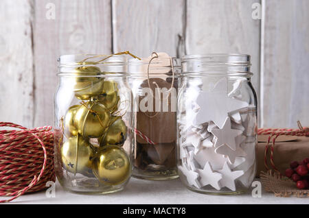 Weihnachtsgeschenk Verpackung liefert. Nahaufnahme der drei Maurer Gläser mit Geschenkanhänger, Holz Sterne, und Schlittenglöckchen gegen eine weiße Wand. Stockfoto