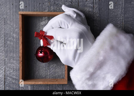 Santa Claus hängt ein roter Jingle Bell in einem Holzrahmen auf grau Holz Wand. Stockfoto