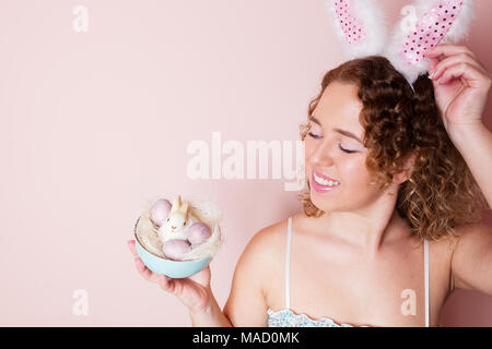 Schöne Frau halten Ostern Dekorationen mit Hasenohren auf rosa Hintergrund mit kopieren. Stockfoto