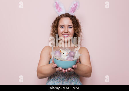 Schöne Frau halten Ostern Dekorationen mit Hasenohren auf rosa Hintergrund mit kopieren. Stockfoto