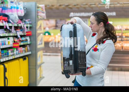 Eine junge Frau wählt einen Koffer für Reisen in die Mall. Stockfoto