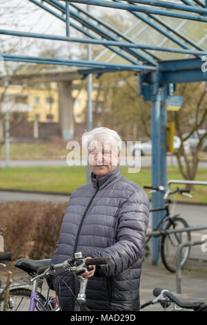 Ältere Frau mit grauen Haaren auf der Bushaltestelle mit Fahrrad Stockfoto