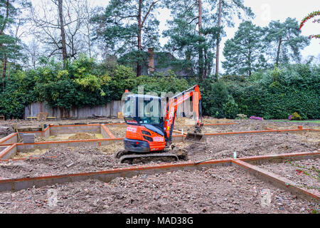 Orange Hitachi schwerem mechanische Digger in den Grundstein für ein neues Haus im Bau auf einer Baustelle in Surrey, Südosten, England, Grossbritannien Stockfoto