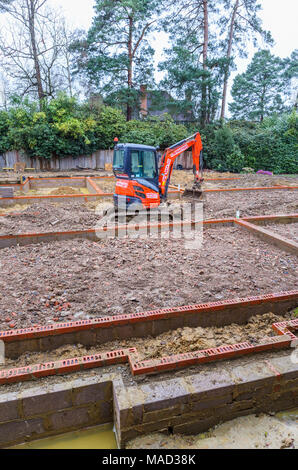 Orange Hitachi schwerem mechanische Digger in den Grundstein für ein neues Haus im Bau auf einer Baustelle in Surrey, Südosten, England, Grossbritannien Stockfoto