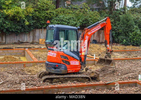 Orange Hitachi schwerem mechanische Digger in den Grundstein für ein neues Haus im Bau auf einer Baustelle in Surrey, Südosten, England, Grossbritannien Stockfoto