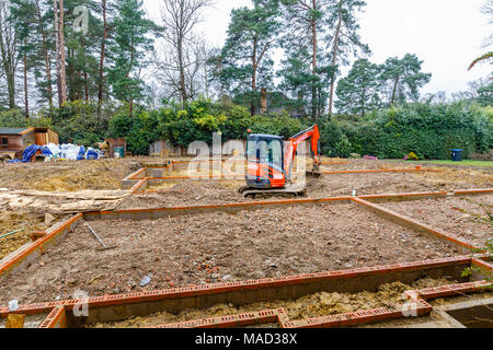 Orange Hitachi schwerem mechanische Digger in den Grundstein für ein neues Haus im Bau auf einer Baustelle in Surrey, Südosten, England, Grossbritannien Stockfoto