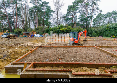 Orange Hitachi schwerem mechanische Digger in den Grundstein für ein neues Haus im Bau auf einer Baustelle in Surrey, Südosten, England, Grossbritannien Stockfoto