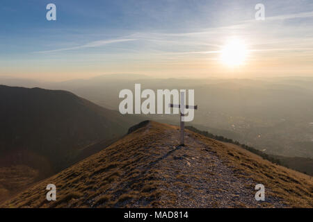 Kreuz auf dem Gipfel des Mt. Serrasanta (Umbrien, Italien), mit warmen goldenen Stunde Farben und die Sonne tief am Horizont Stockfoto