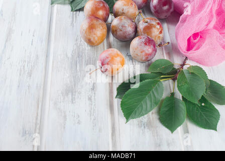 Frische rosa Pflaumen mit Blätter aus dem Garten auf alten hölzernen Tisch verstreut. Viel Platz kopieren Stockfoto