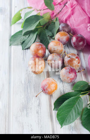 Frische rosa Pflaumen mit Blätter aus dem Garten auf alten hölzernen Tisch verstreut. Viel Platz kopieren Stockfoto
