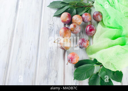 Frische rosa Pflaumen mit Blätter aus dem Garten auf alten hölzernen Tisch verstreut. Viel Platz kopieren Stockfoto