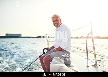 Lächelnd reifer Mann sitzen auf dem Deck des Schiffes genießen Sie einen sonnigen Tag Segeln auf dem offenen Ozean Stockfoto