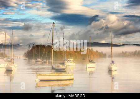 Der Lake District National Park. Cumbria. Die westlichen Ufer des Windermere Blick von der Fähre dock. Am frühen Morgen Nebel mit Booten in den Vordergrund. Stockfoto