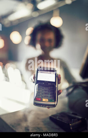 Junge afrikanische Kellnerin präsentiert eine elektronische Karte Payment Terminal, während bei einem Zähler in einem Restaurant stehend Stockfoto