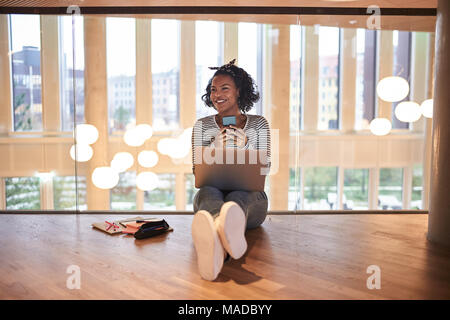 Lächelnde junge afrikanische Studenten sitzen auf einem Campus Stock zwischen den Klassen Lesen von SMS-Nachrichten auf Ihrem Handy und ein Laptop verwenden Stockfoto
