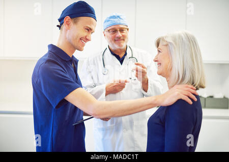 Freundlich lächelnden jungen Arzt Berühren der Schulter der reifen Frau und jubeln Ihr in der Klinik. Stockfoto