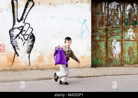 Bilin, Palästina, 31. Dezember 2010: Palästinensische Junge ist zu Fuß auf der Straße von bilin vor V Zeichen Graffiti. Stockfoto