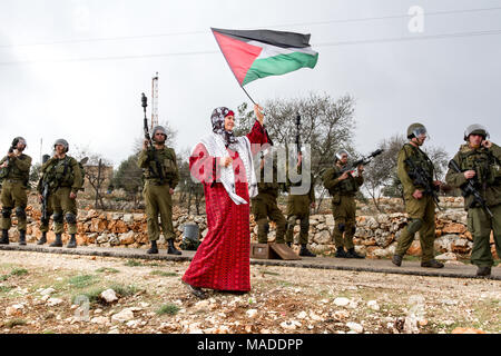 Bilin, Palästina, 31. Dezember 2010: Palästinensische Frau geht mit der palästinensischen Flagge vor Israel Defense Force Soldaten während der wöchentlichen demonstrati Stockfoto