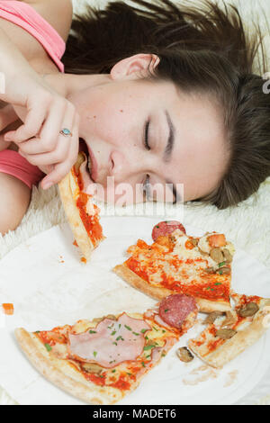 Spaß hungrig Mädchen liegt auf dem Bett isst Pizza Stockfoto