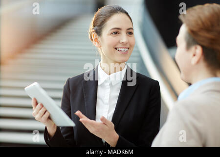 Glückliche junge Mitarbeiter, die Präsentation in der Touchpad während der Interaktion mit älteren Kollegen Stockfoto