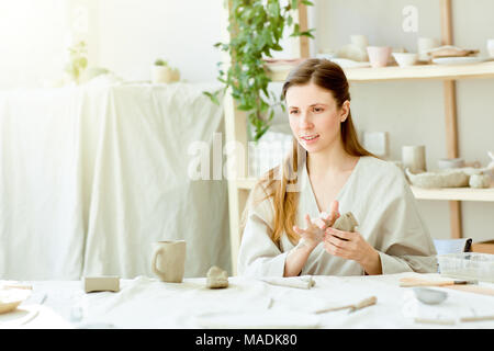 Junge Frau kneten Stück weißer Tonerde, bevor eine andere handgefertigte Artikel in Arbeit studio Stockfoto