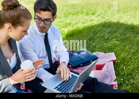 Zuversichtlich Broker und seine Kollegen diskutieren online Daten laptop beim Treffen auf grünem Gras Stockfoto