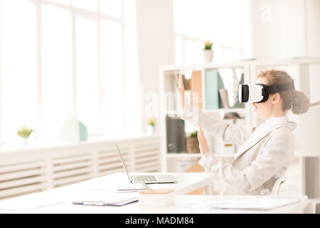 Geschäftsfrau mit Virtual reality Brillen für Laptop und gestikulierend sitzt im Büro Schreibtisch Stockfoto