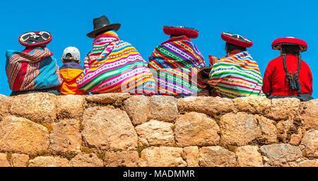 Eine Gruppe von peruanischen Quechua indigene Frauen in traditioneller Kleidung mit einem Jungen auf einem alten Inka Wand in Chincheros in der Nähe der Stadt Cusco, Peru sitzen. Stockfoto