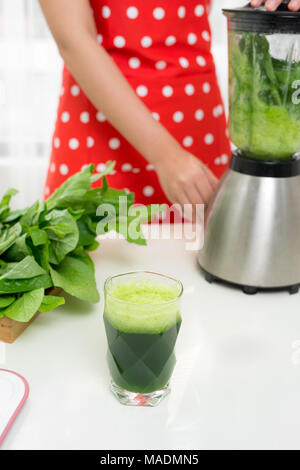 Junge lächelnde Frau Smoothie mit frischen Grüns in den Mixer in der Küche zu Hause. Gesunde vegetarische Smoothie zur Gewichtsabnahme und Entschlackung Stockfoto