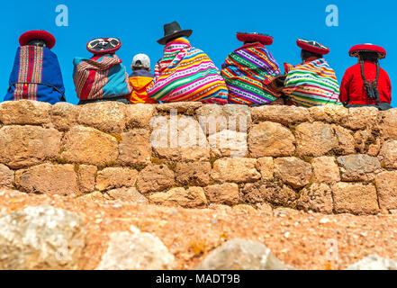 Eine Gruppe von Quechua indigene Frauen und ein Junge auf einem alten Inka Wand in die archäologische Stätte von Chincheros in der Nähe der Stadt Cusco, Peru zu plaudern. Stockfoto