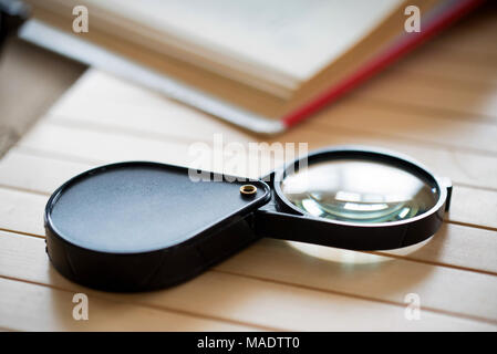 Lupe und offenes Buch auf hölzernen Tabelle schließen Stockfoto